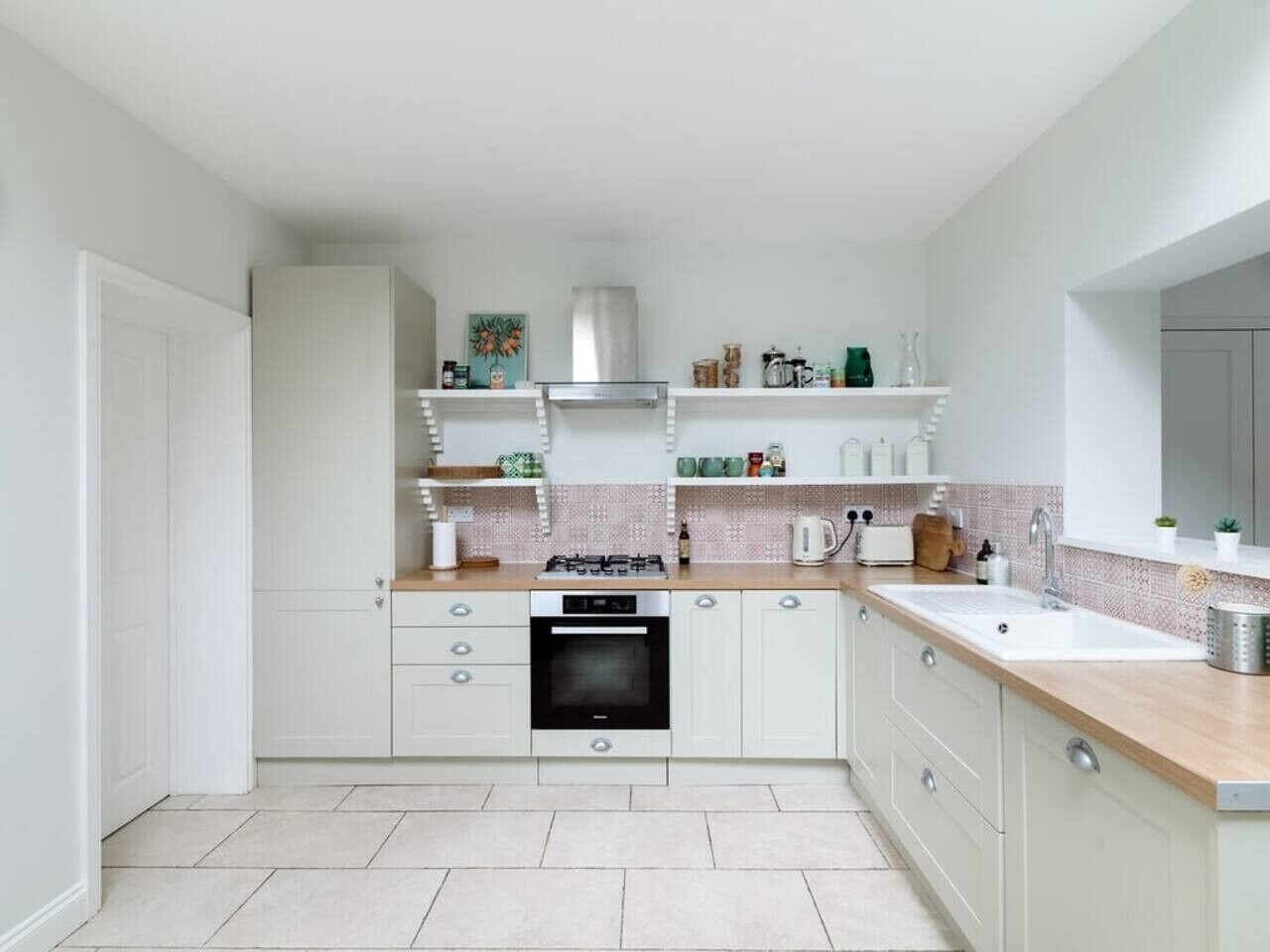 Una cucina moderna con mobili bianchi, piano cottura a gas, forno integrato e un piano di lavoro con diversi utensili da cucina.