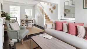 A modern living room with a sofa, armchair, coffee table, and a staircase leading to another level. - Battersea Bright House | Sleeps 4 (London)