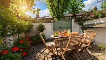 An outdoor patio with a round wooden table and chairs, surrounded by a garden with various plants and flowers.