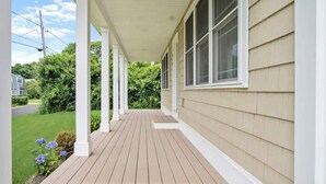 Een overdekte veranda met een houten terras, witte zuilen en beigekleurige bekleding.