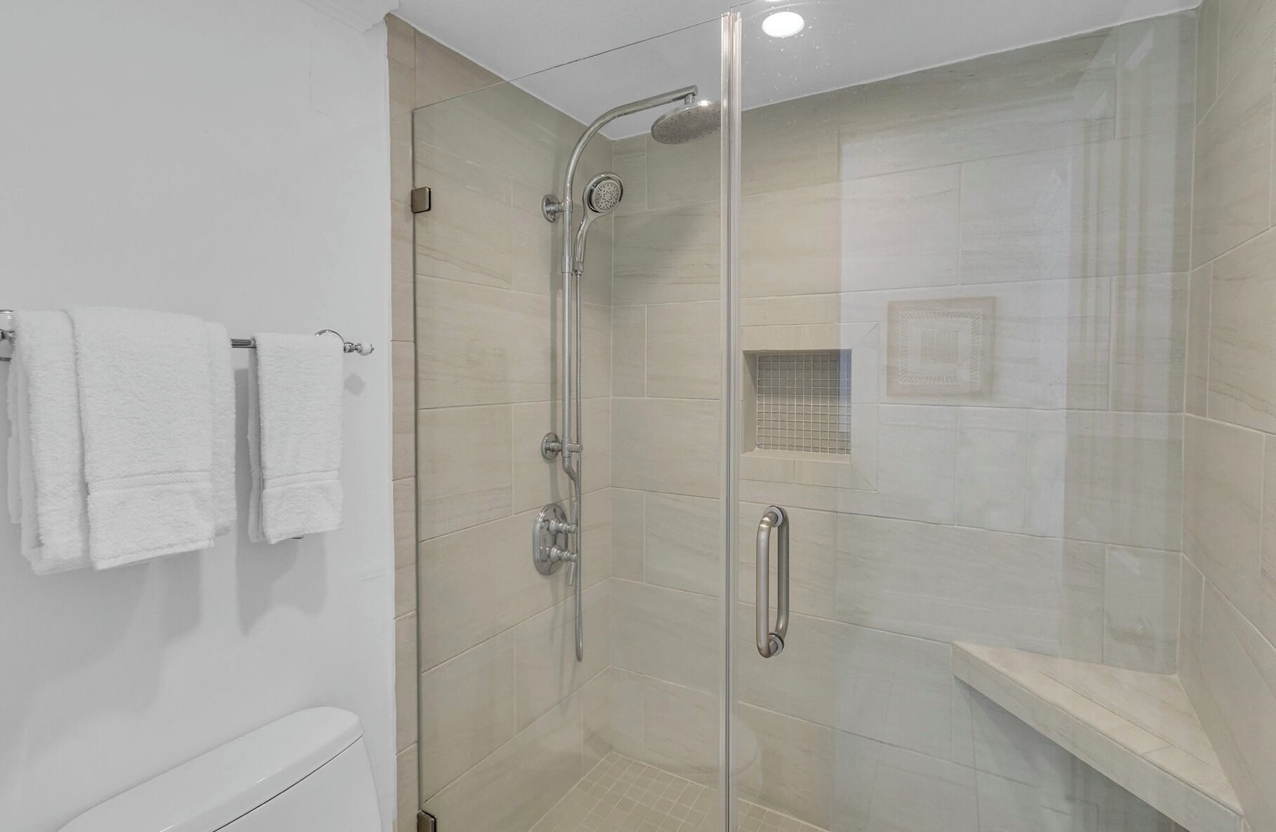 Une douche moderne avec une porte en verre, une barre d’appui et un mur recouvert de carreaux.