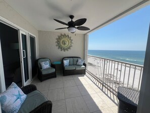 A balcony with wicker furniture, a ceiling fan, and a view of the beach.