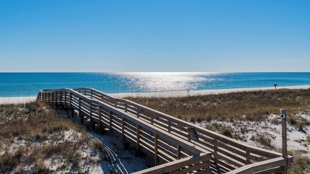 A wooden boardwalk leading to a beach with clear blue water.