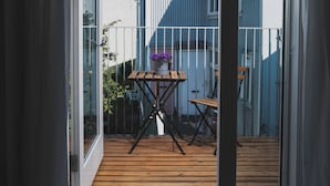 A room with a large sliding glass door leading to an outdoor deck with a wooden table and chairs, a potted plant, and a view of neighboring houses.