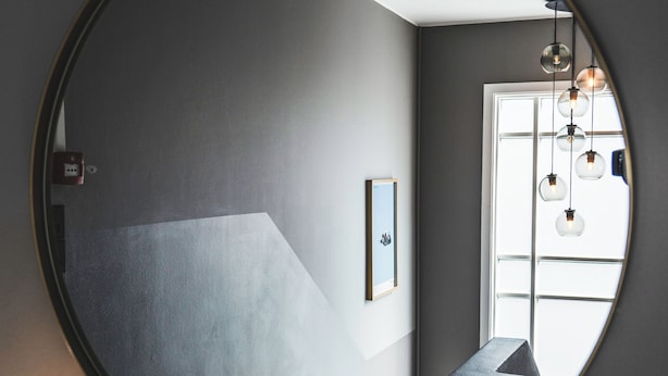 A round mirror reflecting a modern bathroom with a light fixture and a framed picture on the wall.