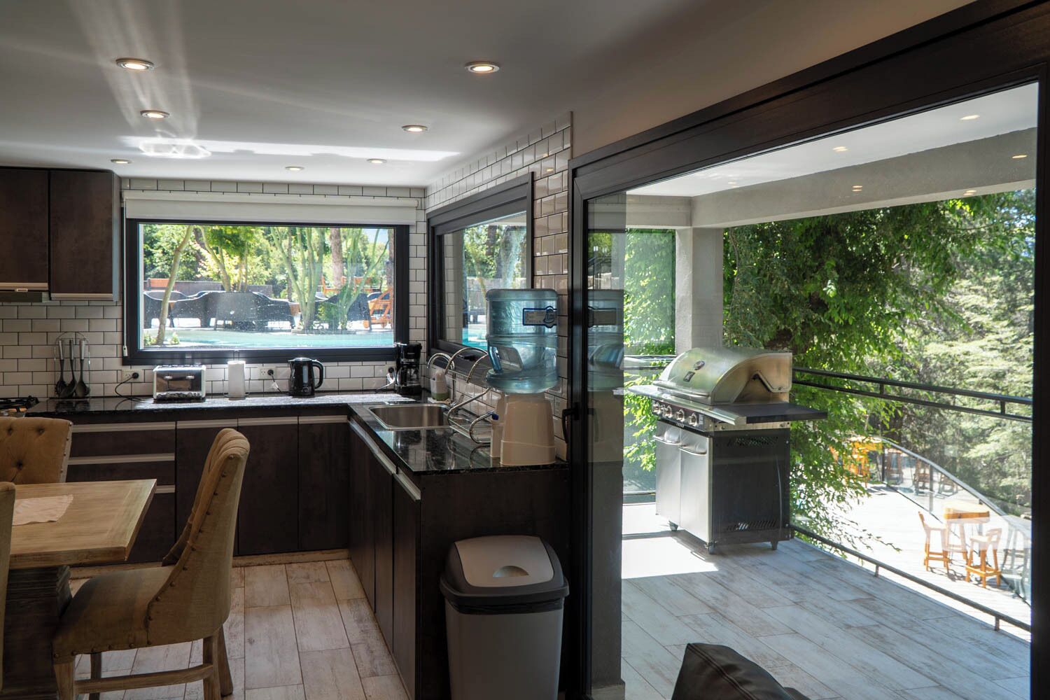 A modern kitchen with a large window, a built-in grill, and a dining area with wooden chairs.