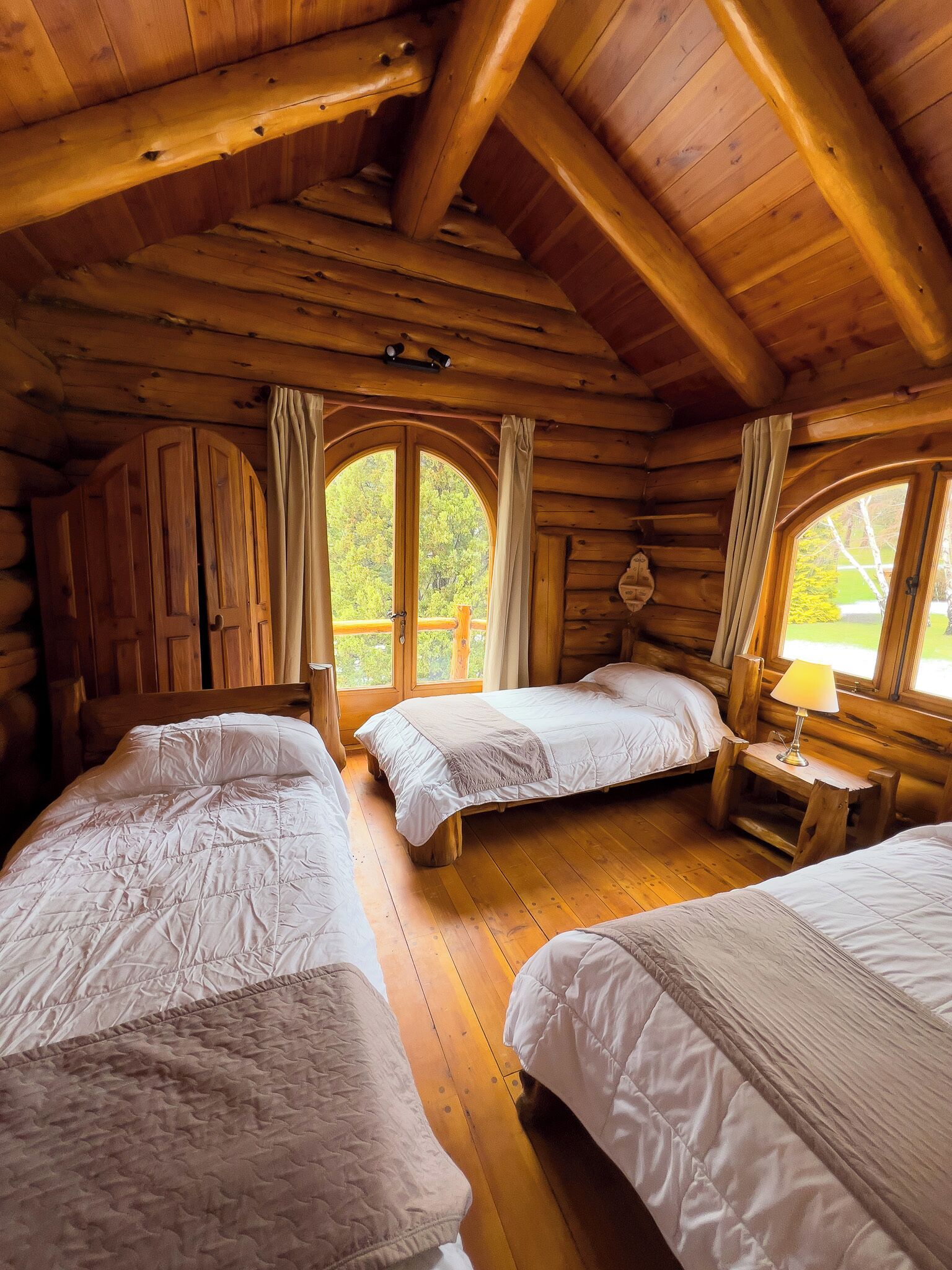 Eine Holzhütte mit drei Betten und großen Fenstern.