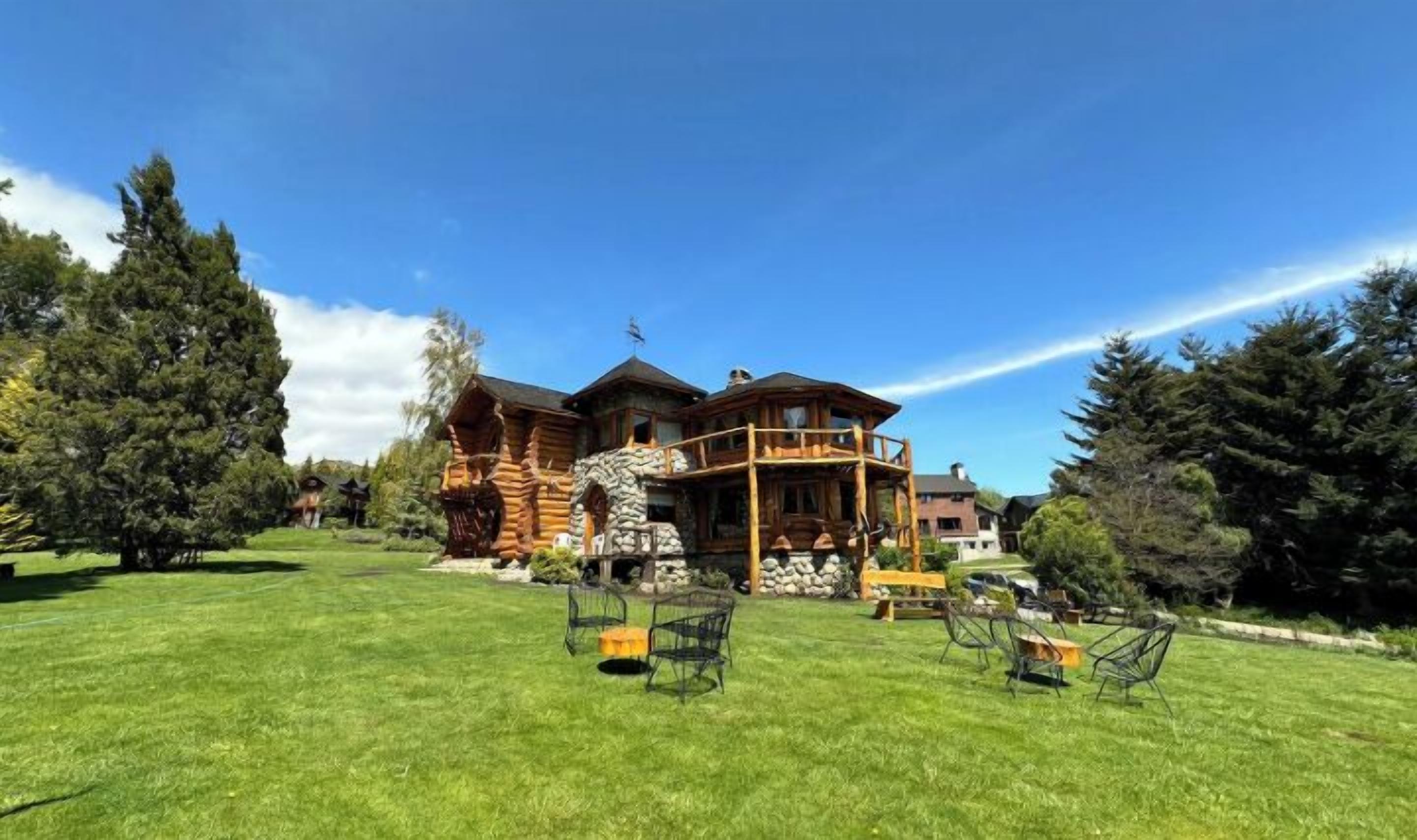 Une grande cabane en rondins, dotée de fondations en pierre, de plusieurs terrasses et d’une pelouse bien entretenue agrémentée de mobilier d’extérieur.