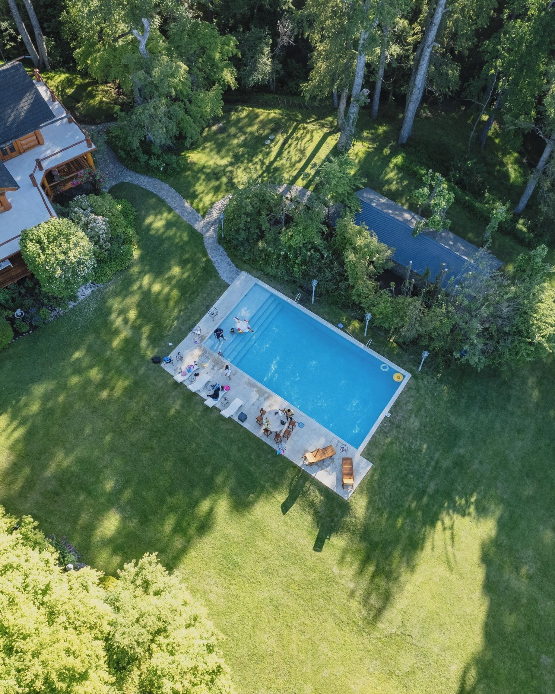 An aerial view of a residential property with a swimming pool, surrounded by lush greenery and a well-maintained lawn.