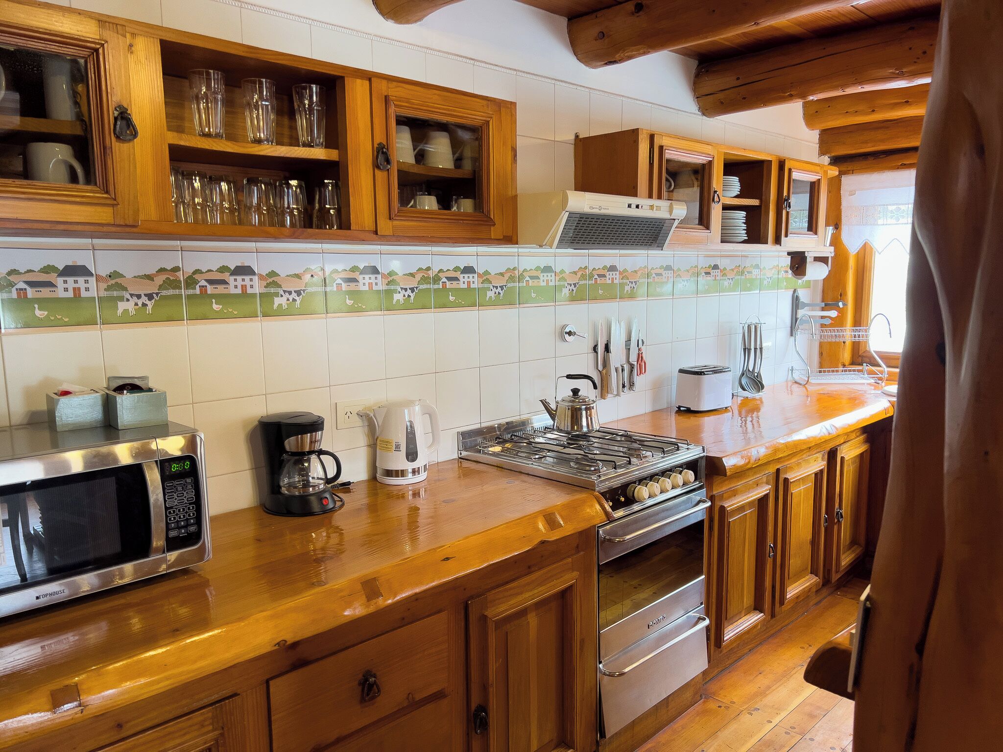 Een keuken met houten kasten, een magnetron, een waterkoker en een fornuis.