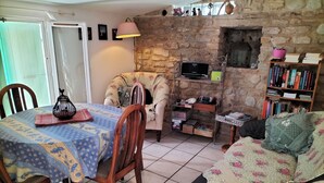 Un salon chaleureux avec un mur en pierre, un téléviseur, une bibliothèque et un coin repas comprenant une table et des chaises.
