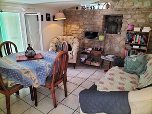 Una sala de estar acogedora con una pared de piedra, televisor, estantería y comedor con mesa y sillas.