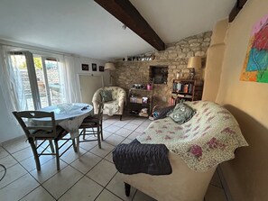A cozy room with a dining table, two chairs, a sofa, a bookshelf, and a stone wall. - Charming 3-bedroom house with Swiming-pool and WiFi in Montbrison-sur-Lez (Montbrison-sur-Lez)