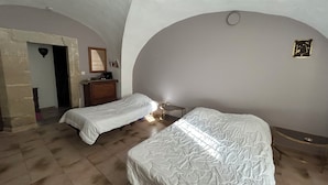 Une chambre avec deux lits, une commode et un miroir. Une porte donne accès à une autre pièce.