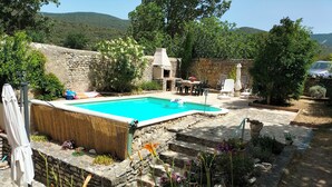 Un espace piscine agrémenté de murs en pierre, de mobilier d’extérieur et offrant une vue sur les collines.