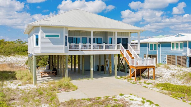 Une maison située en bord de mer, dotée d’un balcon, d’une terrasse et d’un escalier menant à l’étage principal.