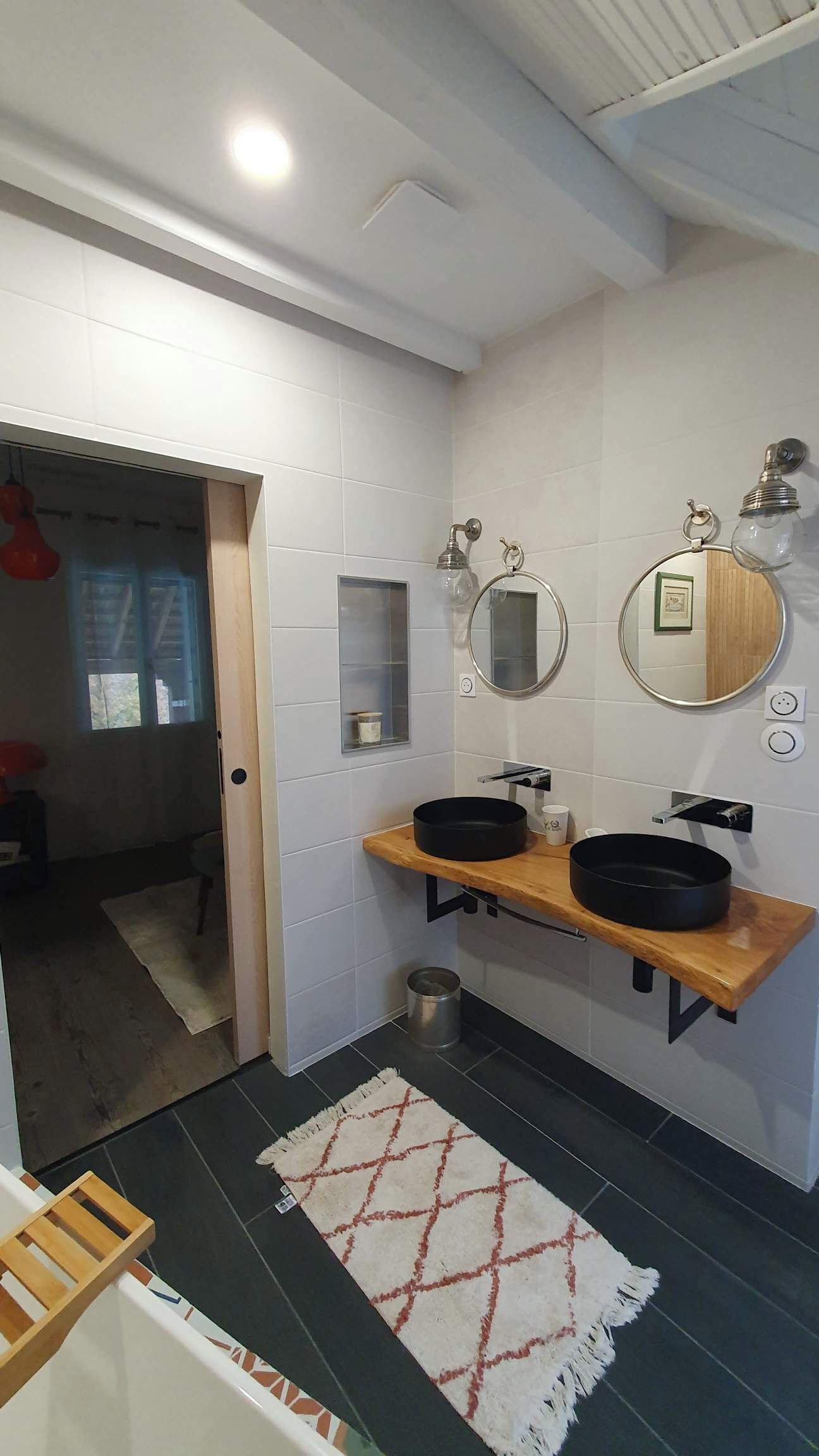 A modern bathroom with two sinks, a mirror, and a small shelf.