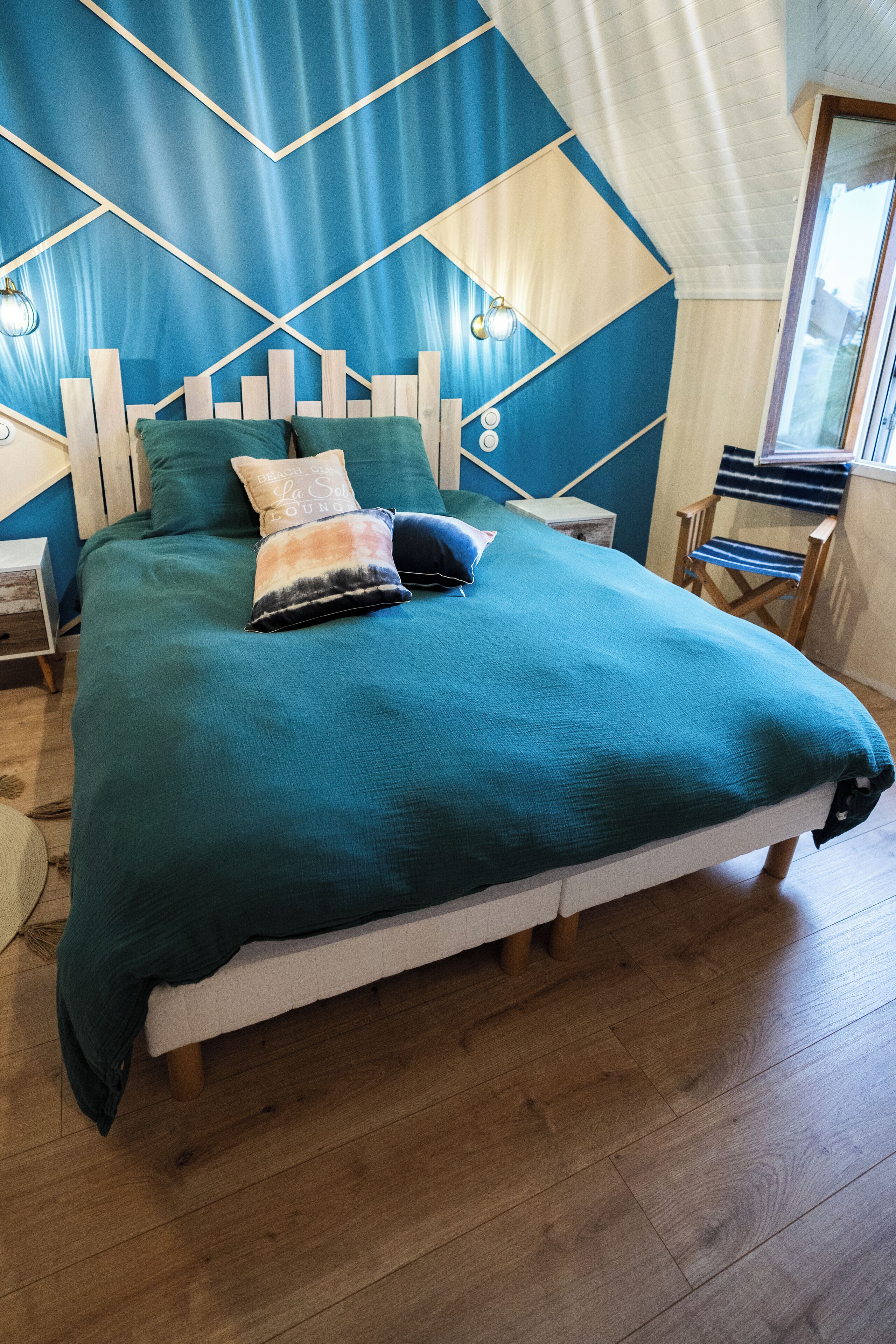 Una cama con una colcha verde azulada, cabecera de madera y dos almohadas.