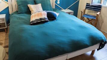 Una cama con una colcha verde azulada, cabecera de madera y dos almohadas.