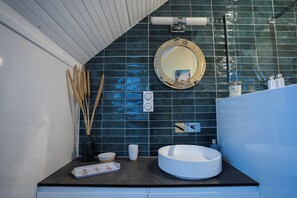 A modern bathroom with a round mirror, a white sink, and a dark tiled backsplash. - La Maison de Judith  (Orthez)