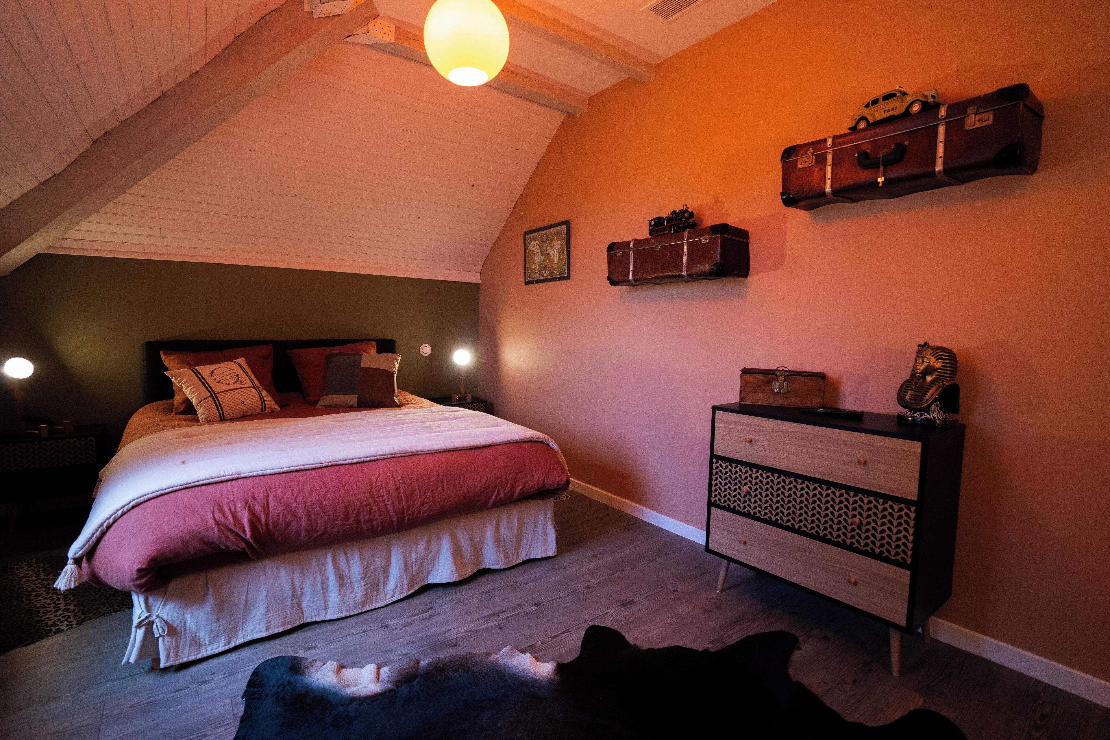 Un dormitorio con cama, cómoda, repisa con equipaje y alfombra de cuero de vaca.