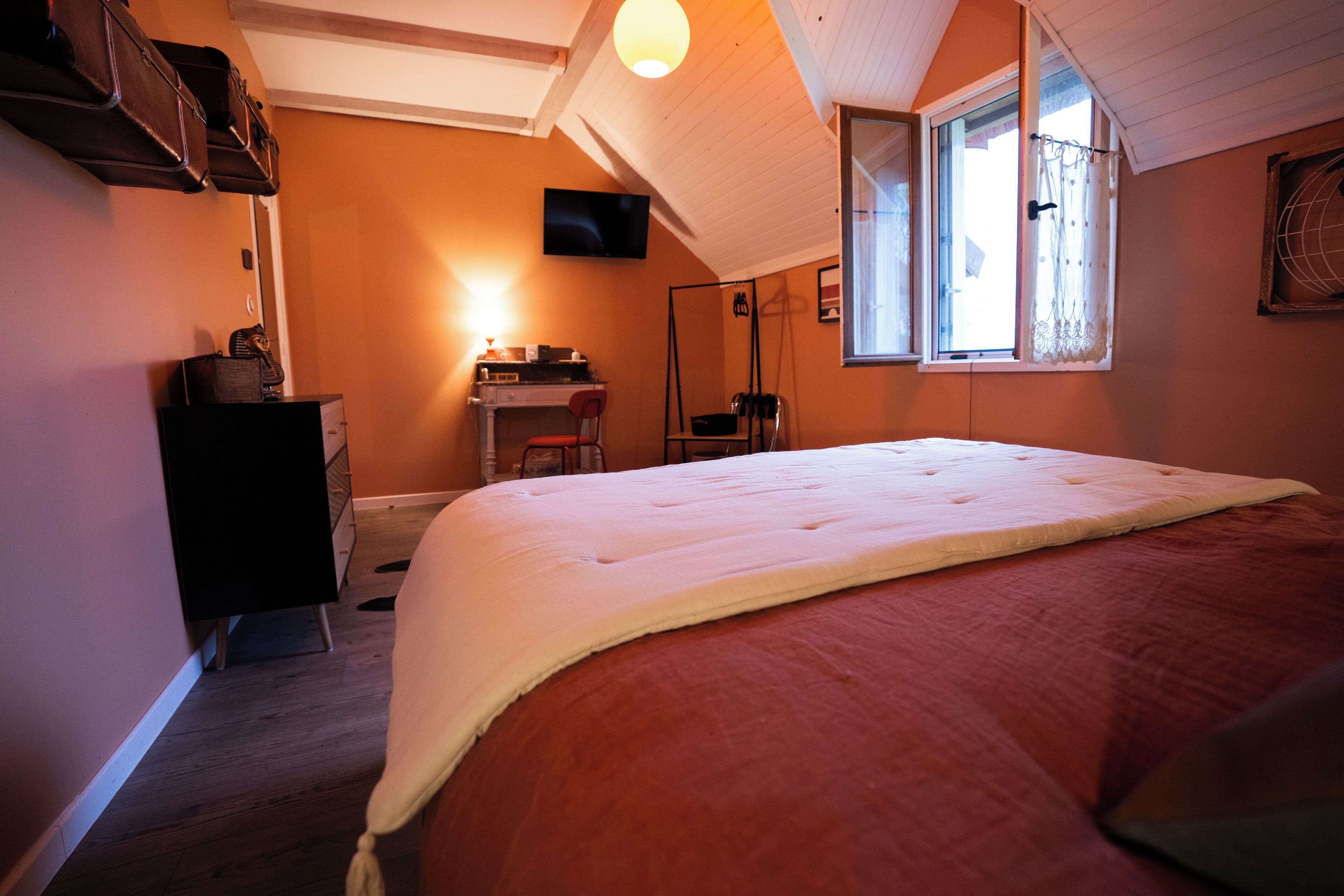 A bedroom with a large bed, a desk, a chair, a television, and a window with curtains.