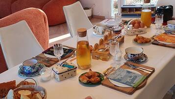 A dining table set with various foods, including bread, pastries, and meats, in a room with a sofa and a view of the outdoors.