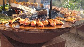 Una parrilla con diversos tipos de carne y verduras asándose al aire libre.