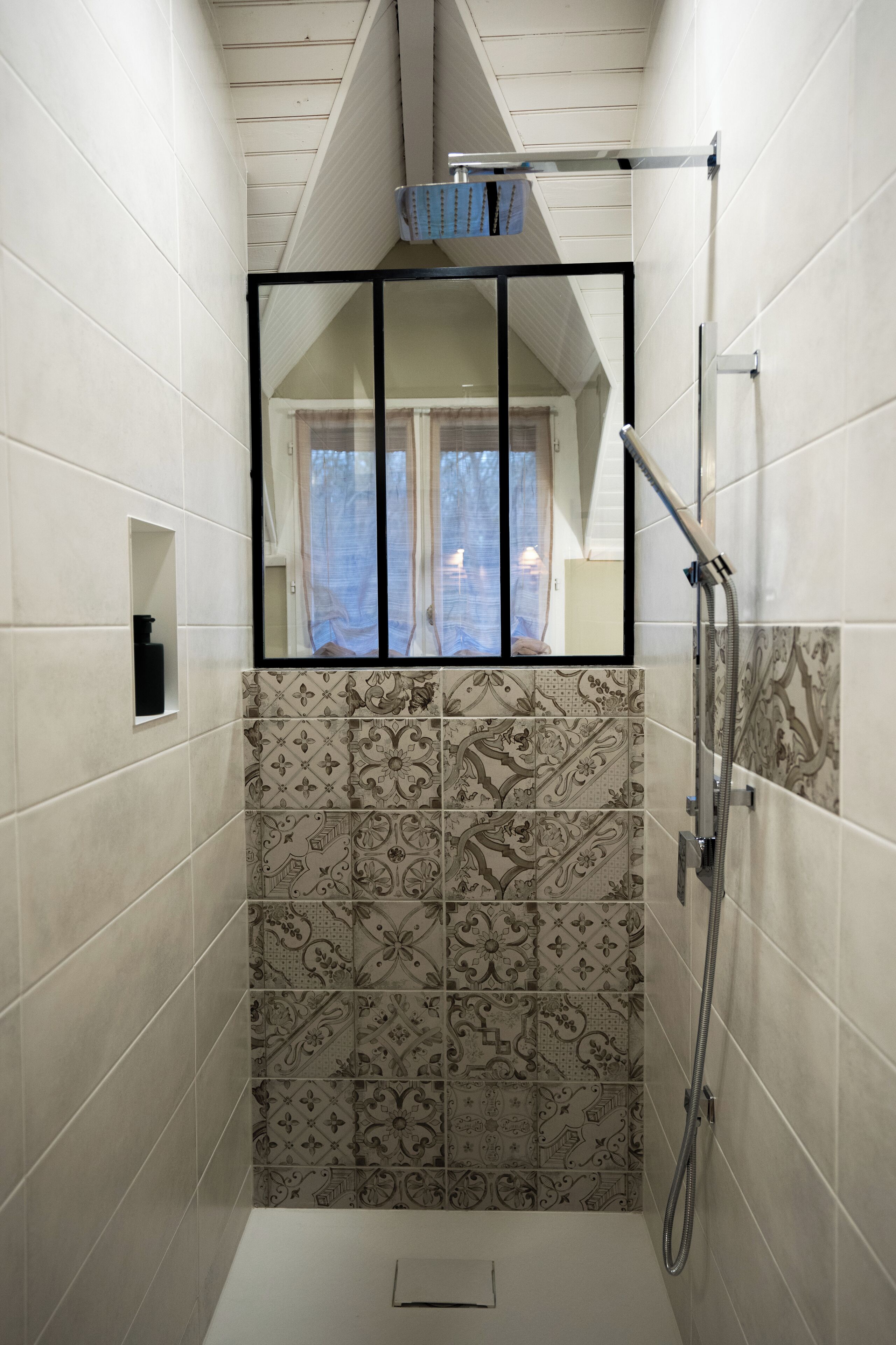 A shower with a window, patterned tiles, and a showerhead.