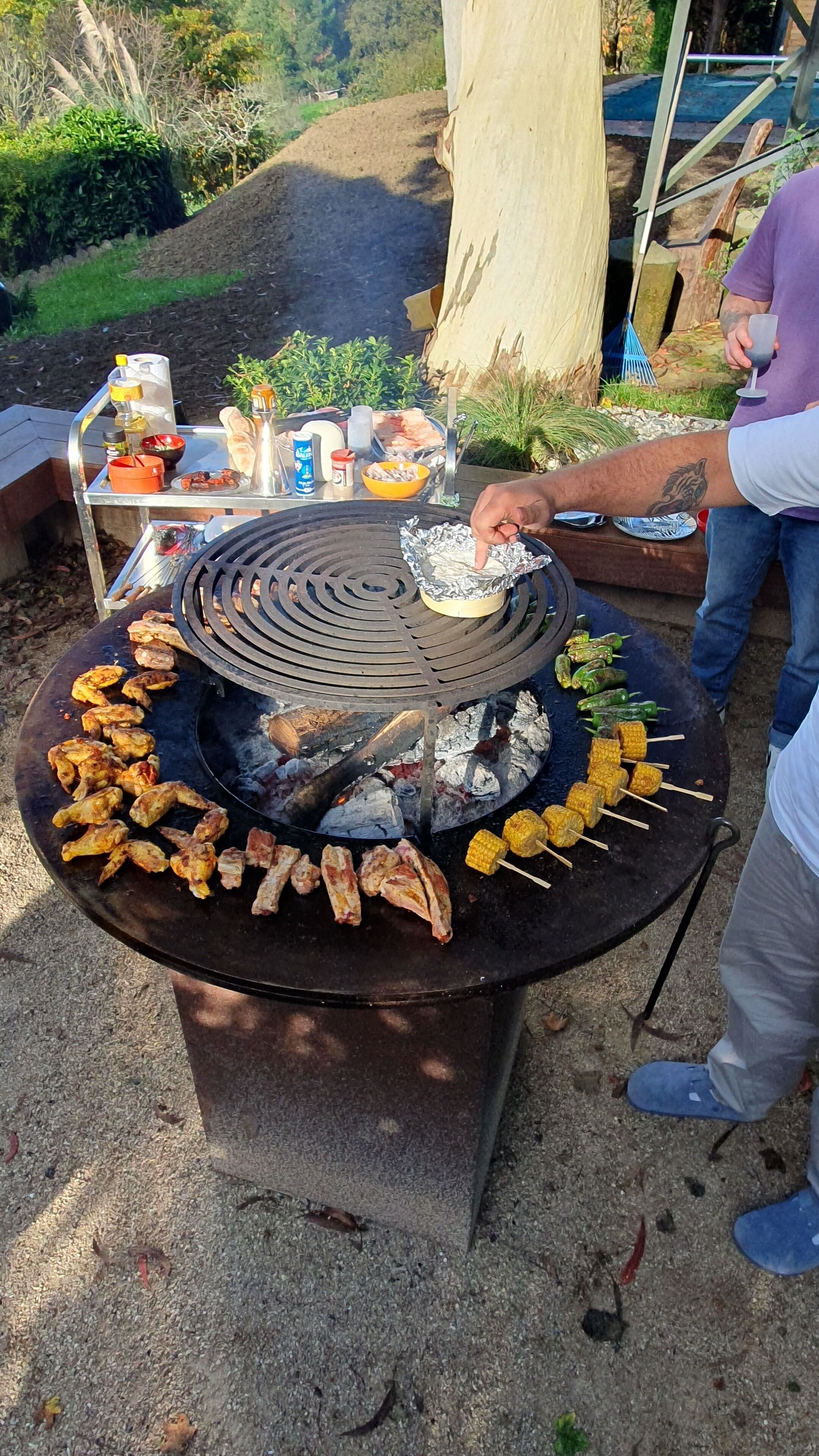 A barbecue grill with various meats and vegetables being cooked.