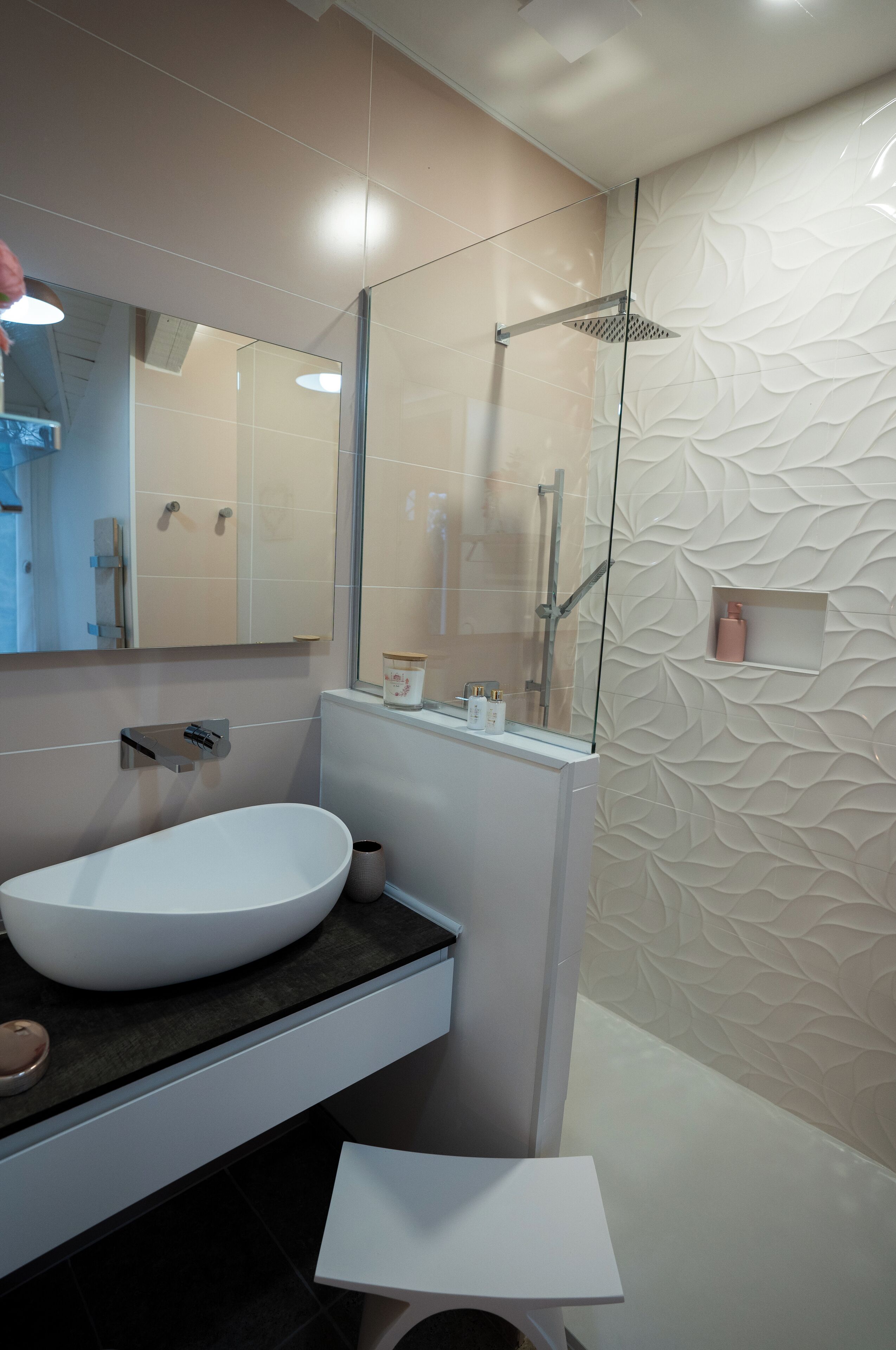 Un baño moderno con un lavamanos ovalado grande, un box de ducha de vidrio y un panel decorativo en la pared.