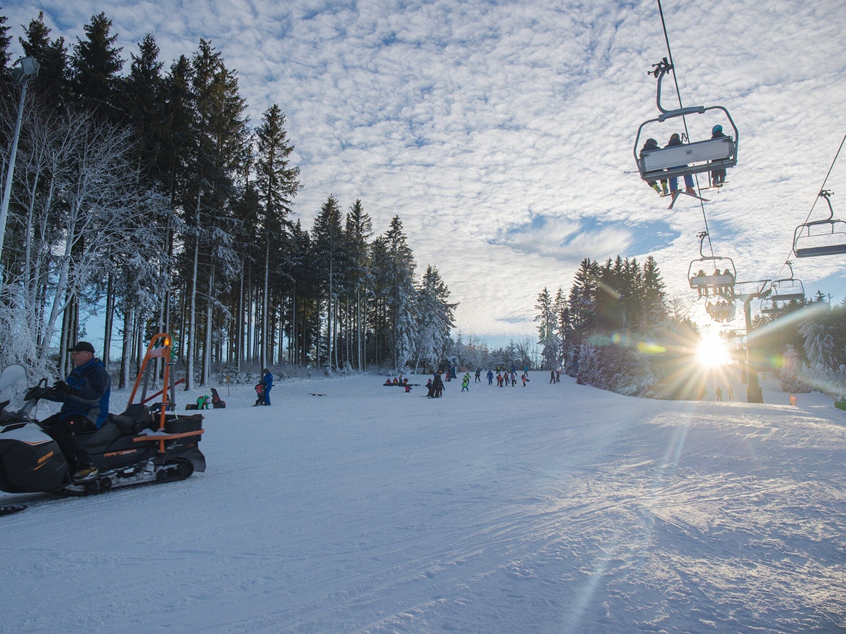 A ski lift with people on it, surrounded by snow-covered trees and a clear sky.