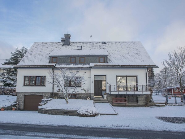 A two-story house with a snow-covered roof, a front porch, and a garage. - Kleine Wohnung in Winterberg mit Tollem Ausblick (Winterberg)