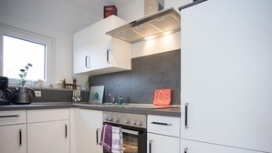 Una cocina moderna con armarios blancos, horno empotrado y una cafetera sobre la encimera.