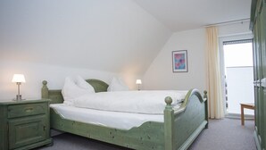 Un dormitorio con una cama individual, una mesita de noche, un aparador y una ventana con cortinas.