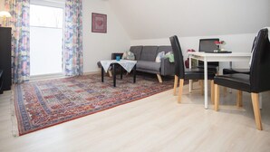 Una sala de estar con sofá, una mesa de comedor con sillas, un tapete estampado y una lámpara en el techo.