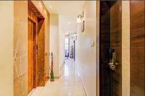 A hallway with a marble floor, wooden doors, and a wall-mounted coffee machine.