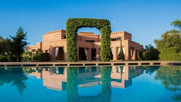 Une piscine dont l’eau reflète clairement un bâtiment doté d’une arche centrale recouverte de verdure.