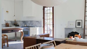 A modern kitchen with a marble countertop, a large white pendant light, and a rustic wooden dining table with a clay pot centerpiece. - This Maine House-Near Ocean! (Tremont)