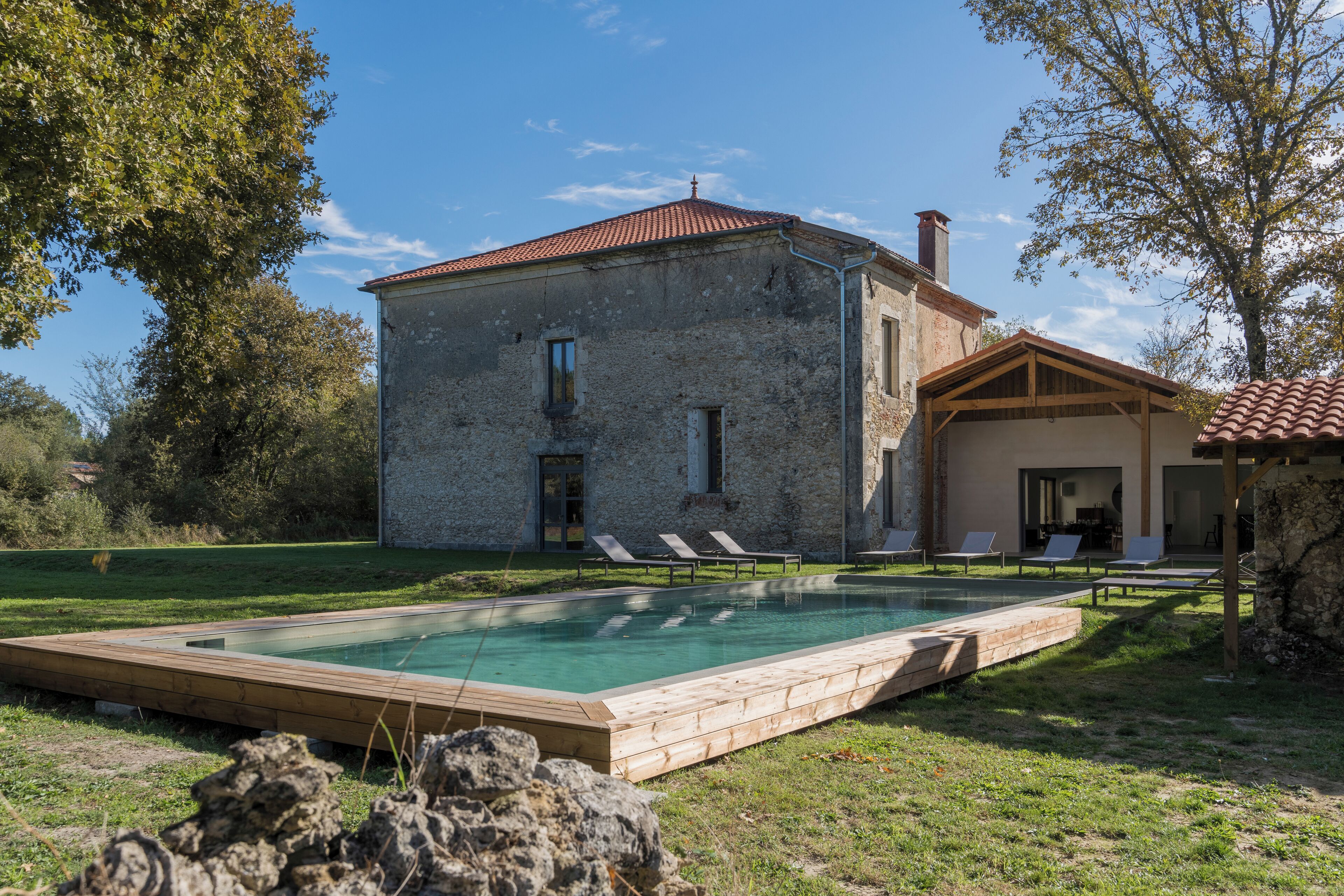 A stone building with a swimming pool, lounge chairs, and a covered patio area.