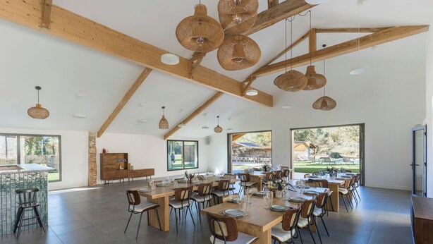 A spacious dining area with high ceilings and exposed wooden beams, featuring multiple tables and chairs arranged for dining. - Large estate renovated with taste and comfort in the heart of nature (Cachen)