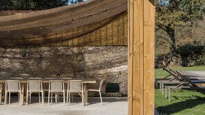 A stone wall with a wooden table and chairs, a woven canopy, and a stone fireplace. - Large estate renovated with taste and comfort in the heart of nature (Cachen)