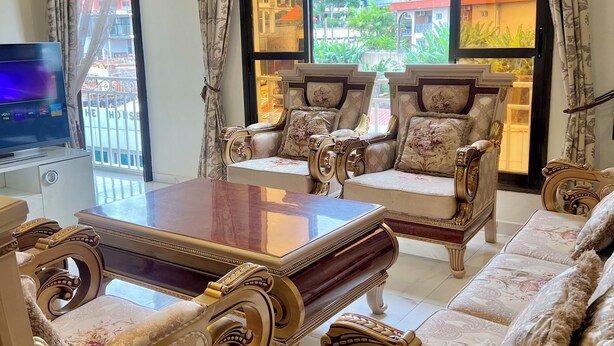 A luxurious living room with ornate furniture, a large window with a view of buildings, and a flat-screen TV. - Lorena House, furnished apartment (Yaoundé)