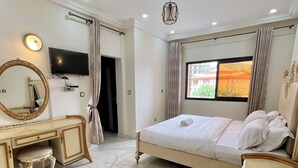A hotel room with a bed, a vanity with a mirror, a television, and a window with curtains. - Lorena House, furnished apartment (Yaoundé)