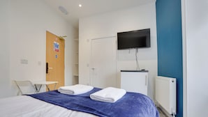 A hotel room with a bed, a TV mounted on the wall, a white door, and a blue accent wall. - Homesly Guest Rooms - 1 Bed Room Apt. (Berwick-upon-Tweed)