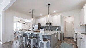 A modern kitchen with white cabinets, stainless steel appliances, and a central island with bar stools. - Bay Breeze Retreat- So Close To All The Fun! Game Room! XL Home! (Orange Beach)