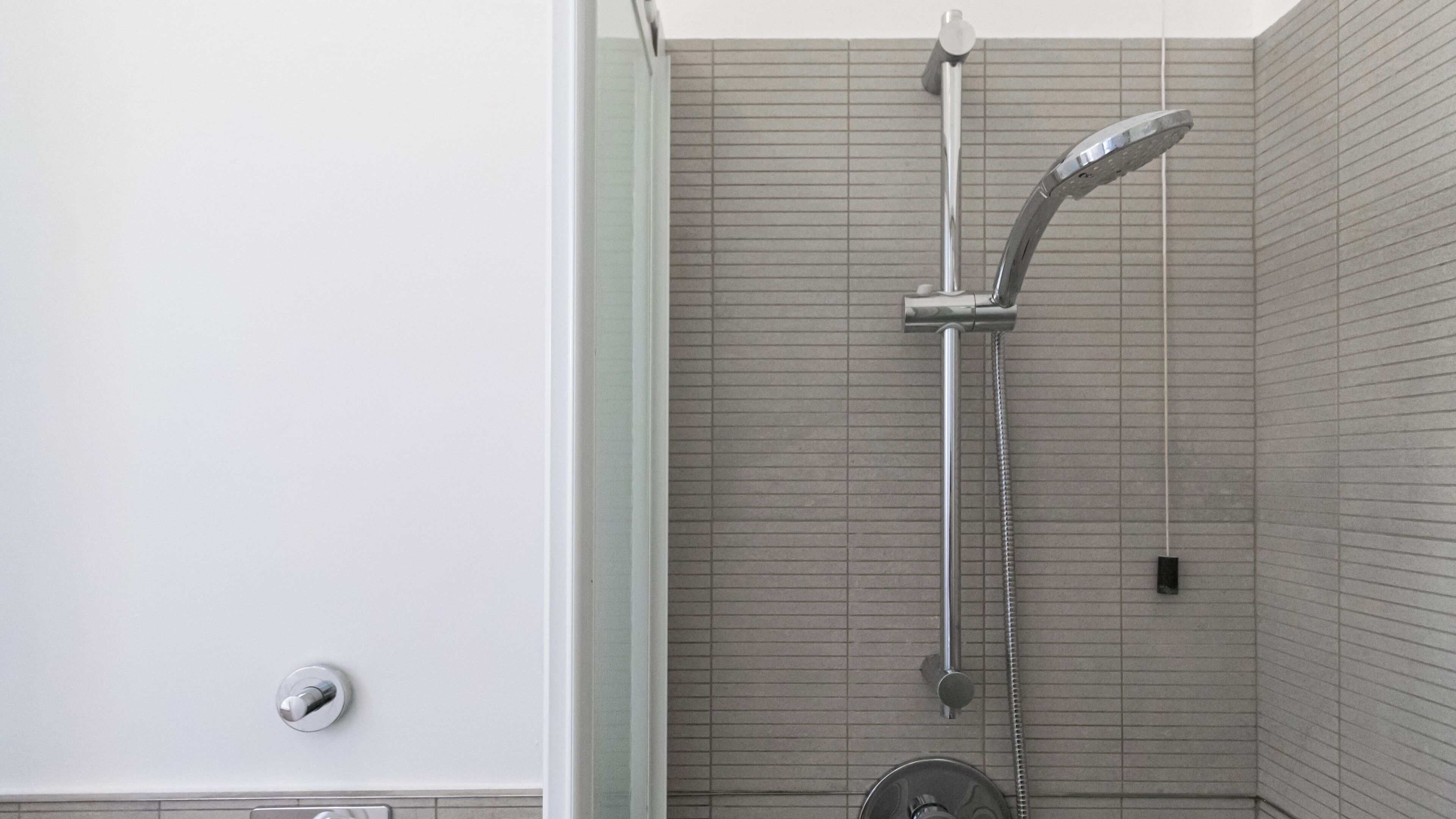 A shower with a handheld showerhead and a wall-mounted faucet in a tiled bathroom.