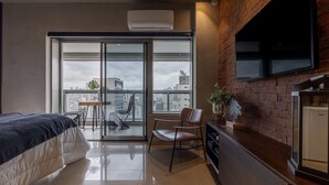 Une chambre d’hôtel moderne équipée d’un lit, d ’une chaise, d’une petite table, d’un téléviseur et d’une grande fenêtre donnant sur la ville.