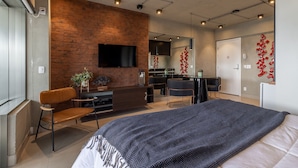 Une chambre moderne avec un grand lit, un bureau et un téléviseur fixé au mur, qui est en briques.