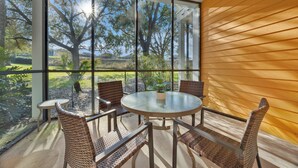 Un patio con paredes de vidrio, mobiliario de mimbre y vista a un paisaje arbolado.